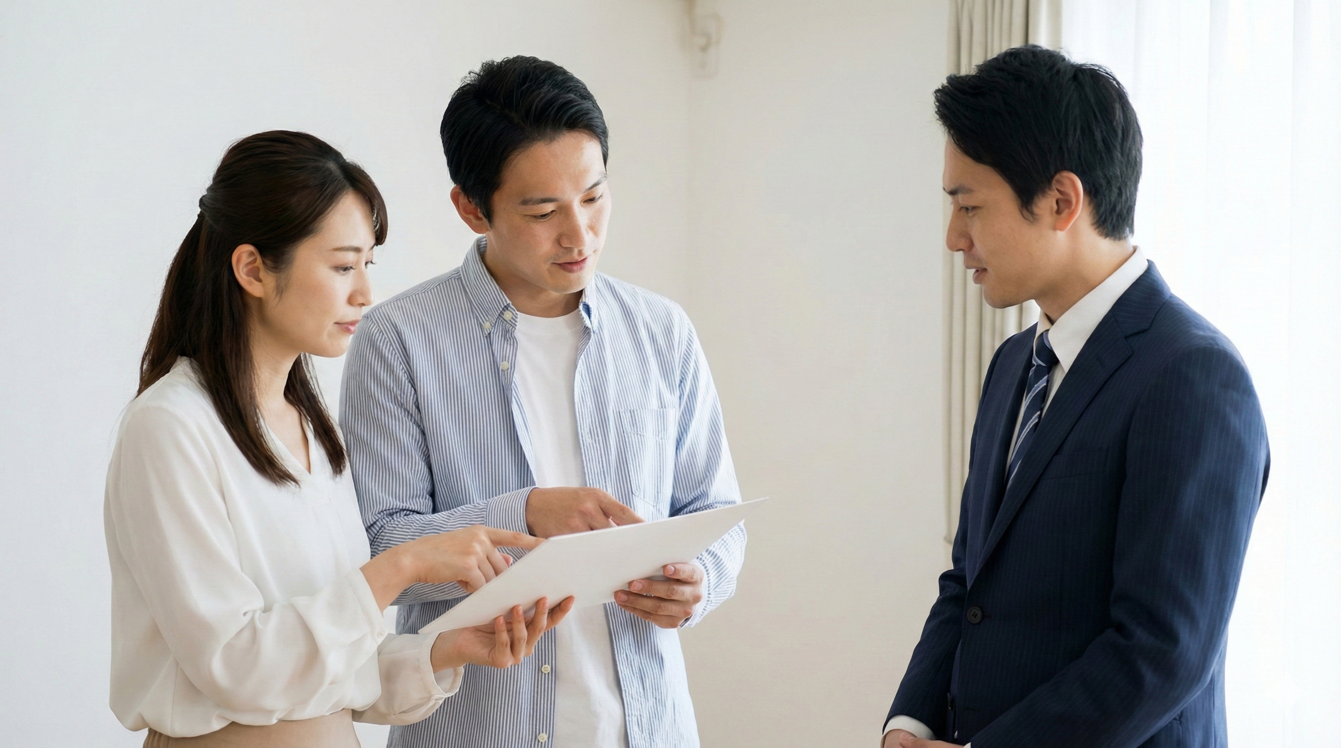 住宅展示場のモデルハウスで、営業担当者に全館空調や床暖房のコスト・メンテナンスについて質問し確認する夫婦。